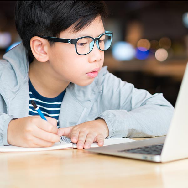 school boy taking notes, working from a laptop computer